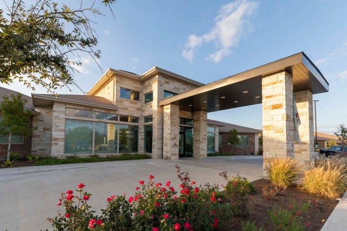 A modern building with a stone facade and large windows, surrounded by landscaping on a sunny day.