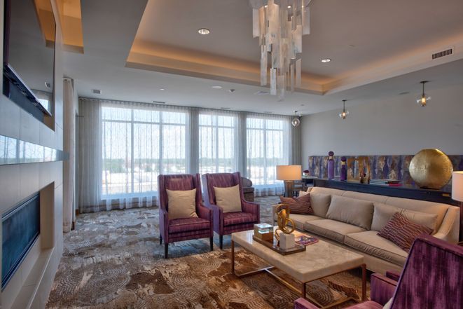 A modern living room with elegant furnishings, featuring a chandelier, plush seating, and ample natural light.