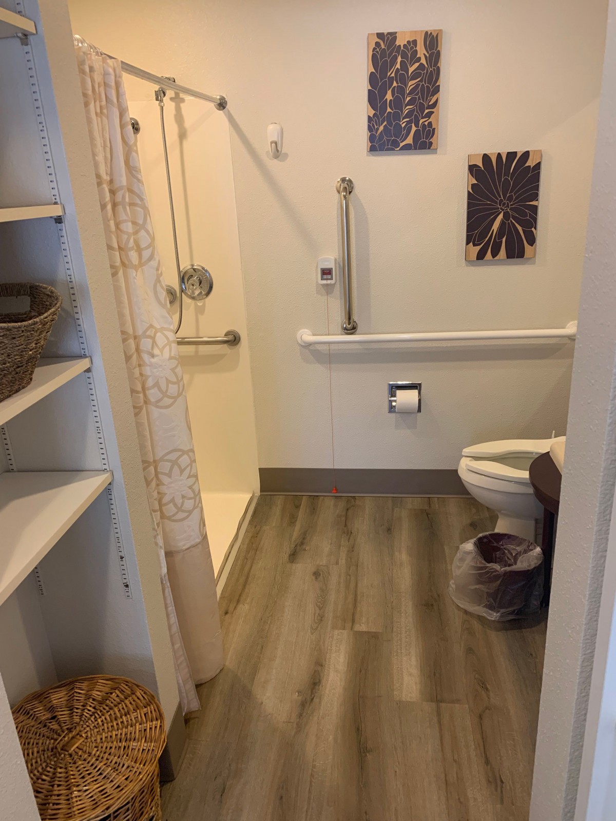 An accessible bathroom with a shower, toilet, and handrails.