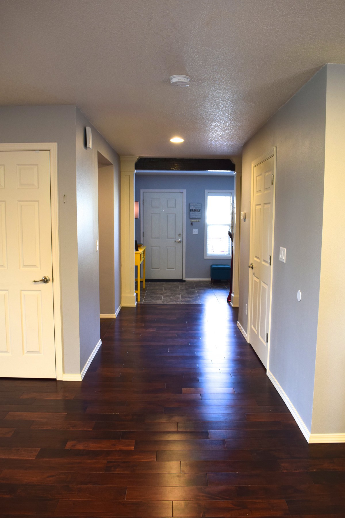 A view of a residential hallway with wooden flooring and light gray walls.