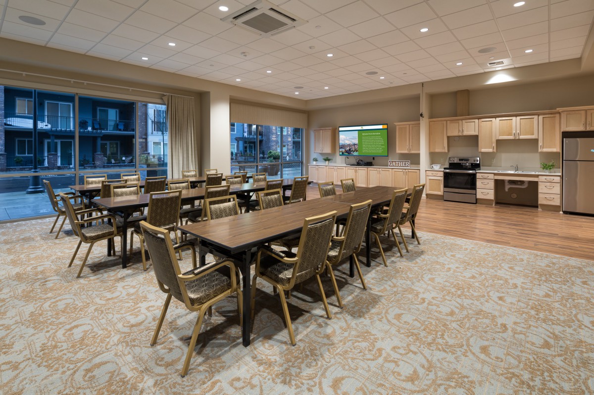 A spacious conference room with tables and chairs, featuring a kitchen area and modern amenities.