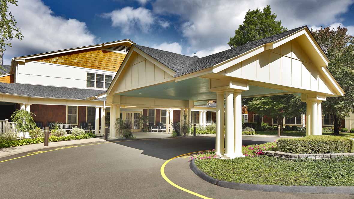 A covered entrance to a large building with columns and a circular driveway.