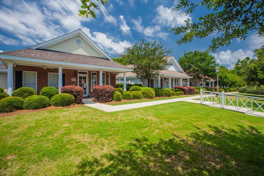 A picturesque residential house with a well-manicured lawn and lush green bushes under a partly cloudy sky.