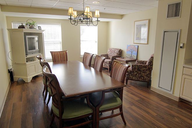 A well-lit dining area with a large wooden table surrounded by chairs, featuring a chandelier and adjacent living space.