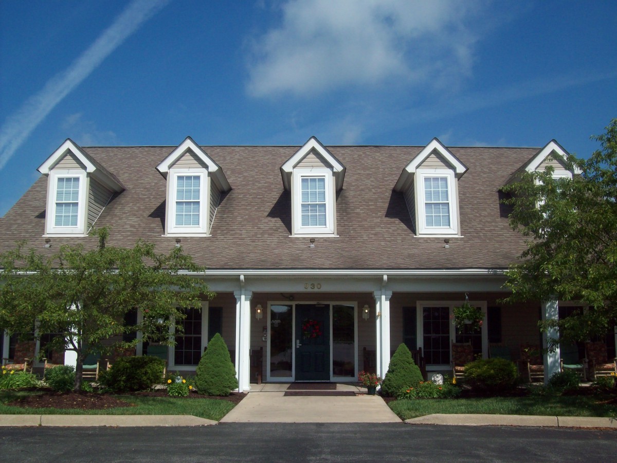 A suburban house with a porch and dormer windows on the roof under a clear blue sky.