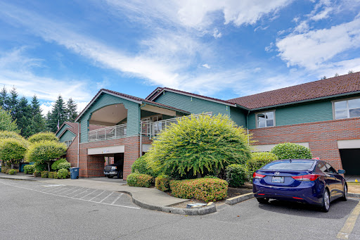A peaceful residential apartment building surrounded by lush greenery under a partly cloudy sky.