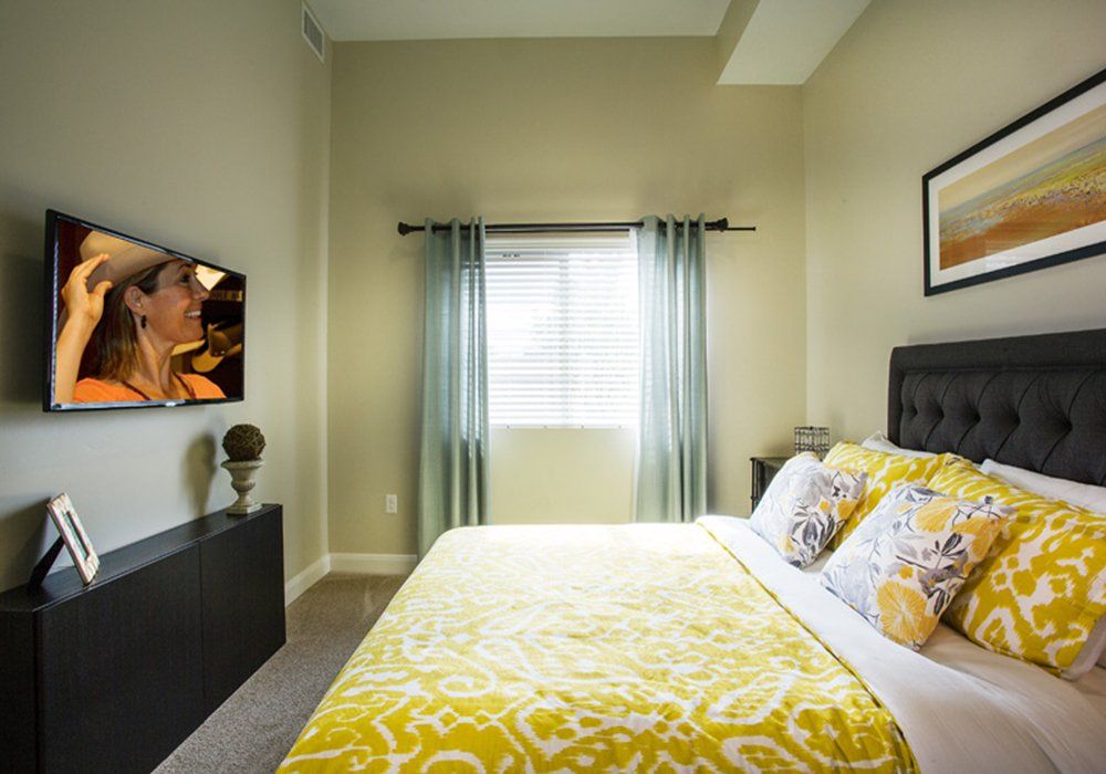 A cozy bedroom with bright yellow bedding and a wall-mounted TV.