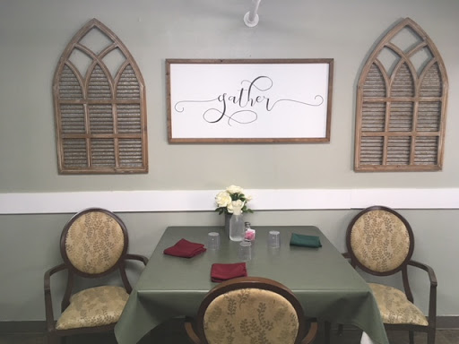 A cozy dining area featuring a green table, decorative chairs, and a welcoming 'gather' sign on the wall.