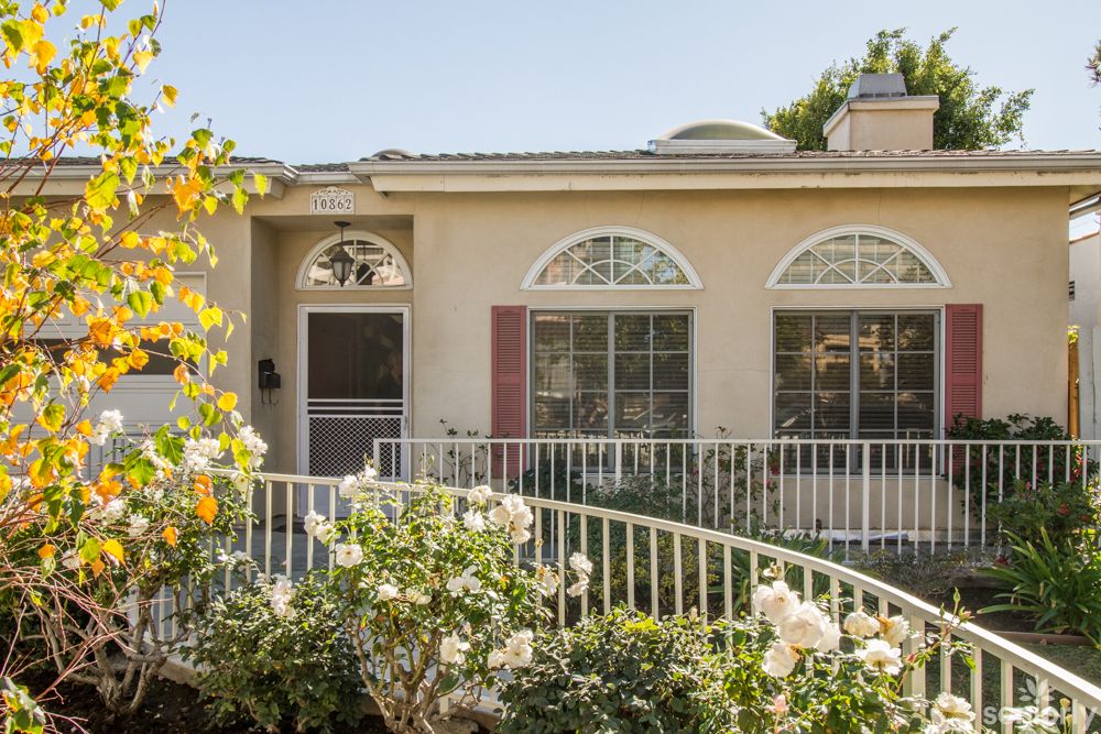 A charming single-story house with large windows and a blooming garden.