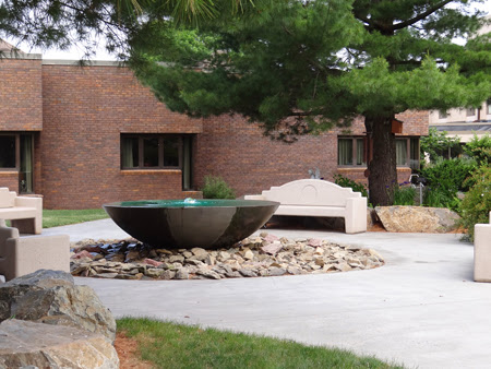 A contemporary fountain surrounded by rocks and greenery in an outdoor setting.