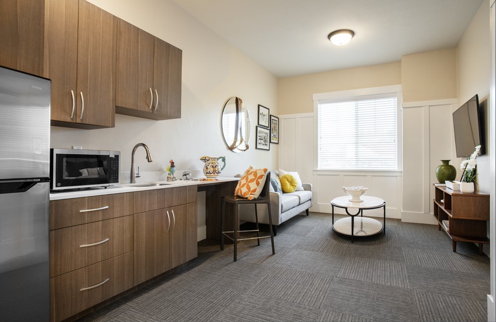 A modern apartment living area featuring a small kitchenette, sofa, and coffee table with stylish decor.