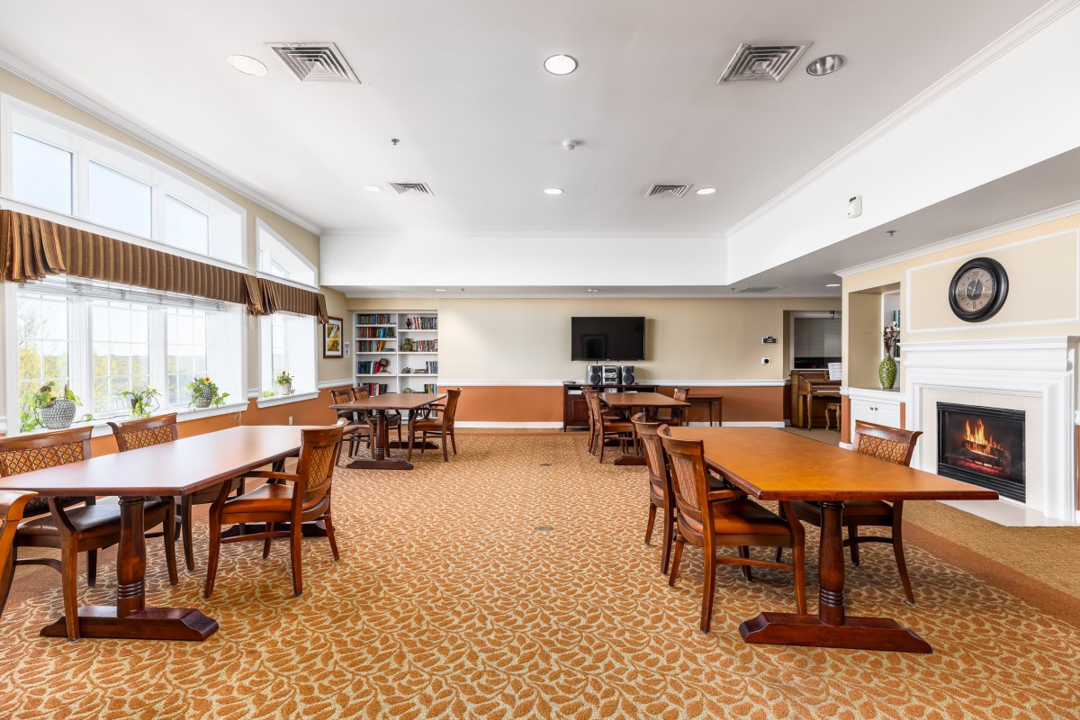 A spacious room with tables and chairs, featuring a television and bookshelves.