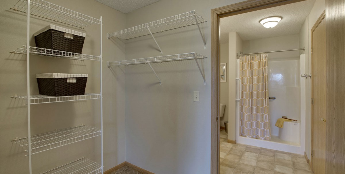An empty walk-in closet with wire shelving and a view into an adjoining bathroom.