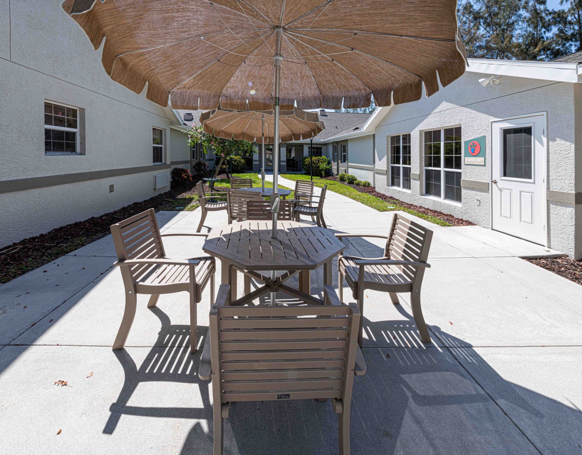 A sunny outdoor patio area with a table, chairs, and an umbrella.