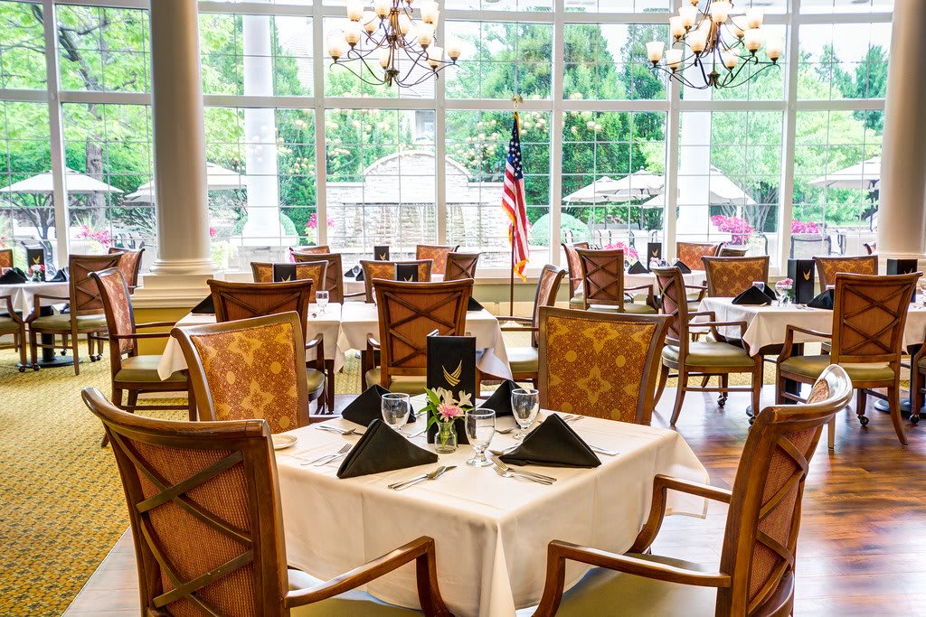 An elegant dining area with neatly arranged tables and chairs, featuring large windows that let in ample natural light.