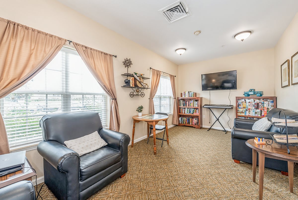 A cozy living room featuring leather chairs, a bookshelf, and a keyboard, with curtains framing the windows.