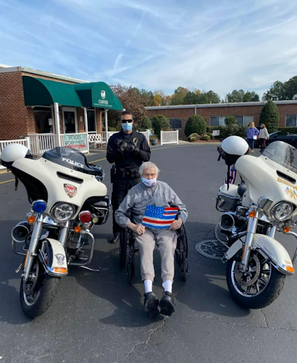 A heartwarming moment as an elderly man enjoys a visit from police officers by their motorcycles outside a healthcare facility.