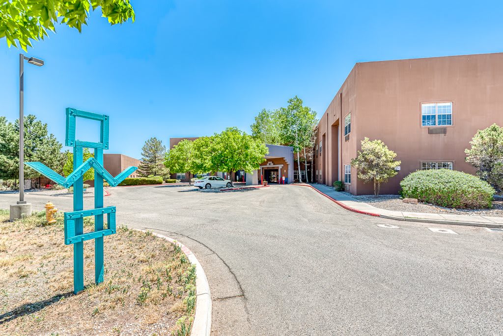 A modern building with a unique sculpture at the entrance, surrounded by trees and a clear blue sky.