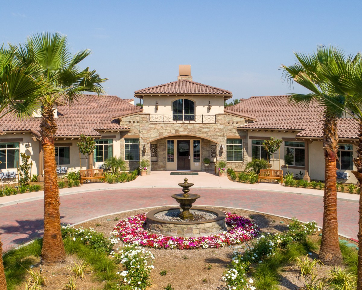 A luxurious building with a central fountain, surrounded by palm trees and vibrant flowers.