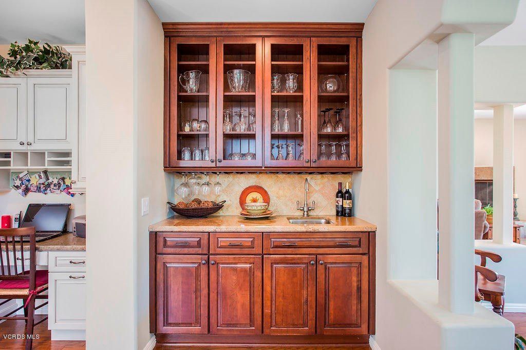 A home bar area with wooden cabinets, glassware, and wine bottles on a countertop.