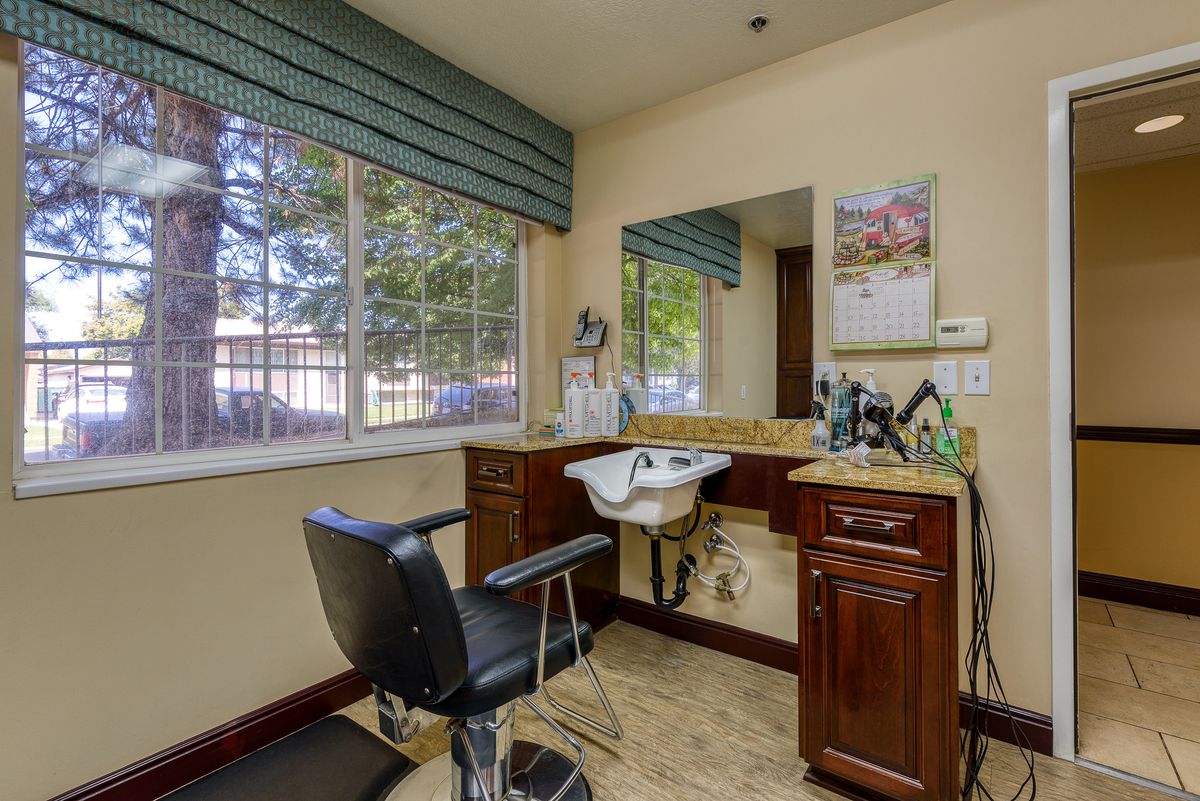 A cozy hair salon corner featuring a barber chair, sink, mirror, and wooden cabinets by a large window.