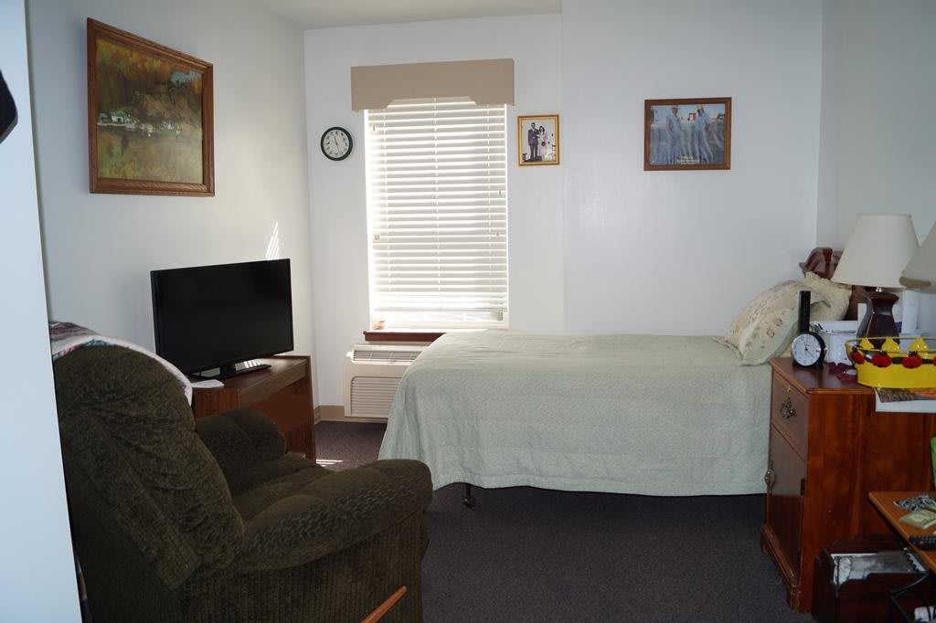 A bedroom with a bed, television, and a comfortable chair.