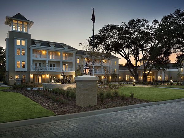 An illuminated hotel building with a landscaped entrance at dusk.
