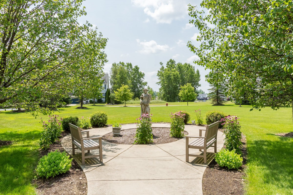 A scenic park view featuring a pathway surrounded by benches and lush greenery.