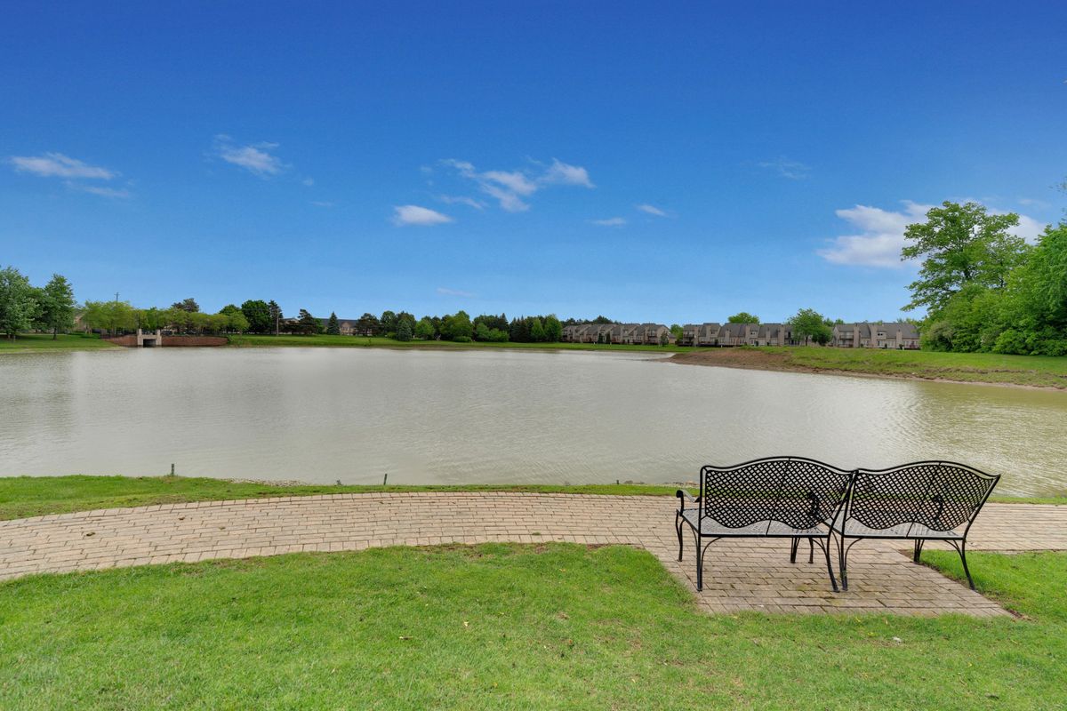 A peaceful view of a lake with a bench on the grassy shore under a clear blue sky.