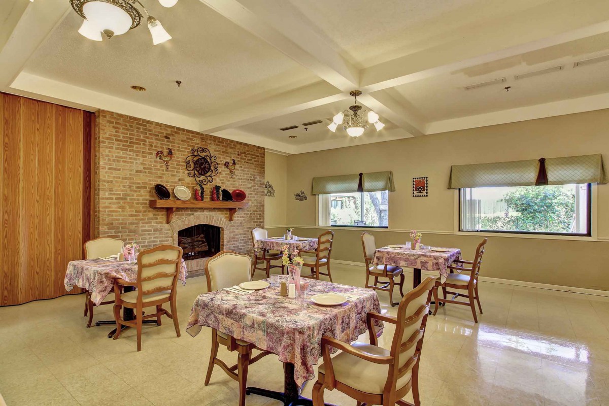 A cozy dining room with multiple tables and chairs, featuring a brick fireplace and ceiling fan.