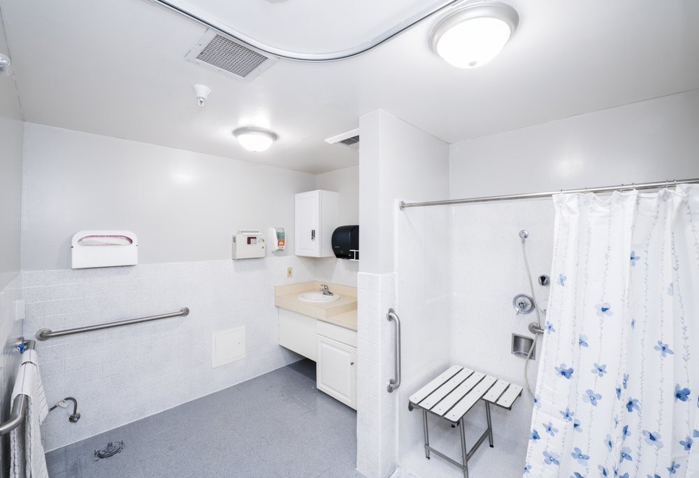 A modern, accessible bathroom featuring a shower with a chair and grab bars.