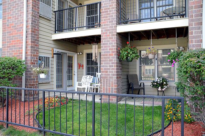 An apartment with balconies and a small fenced lawn, featuring outdoor seating and hanging plants.
