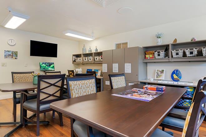 A well-organized office meeting room featuring a large conference table, chairs, shelves filled with books, and a TV screen on the wall.
