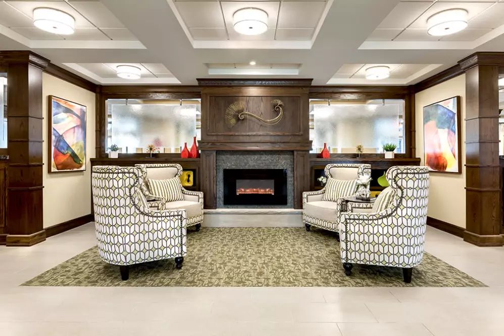 A cozy living room with patterned armchairs and a central fireplace, enhanced by elegant wood paneling and soft lighting.