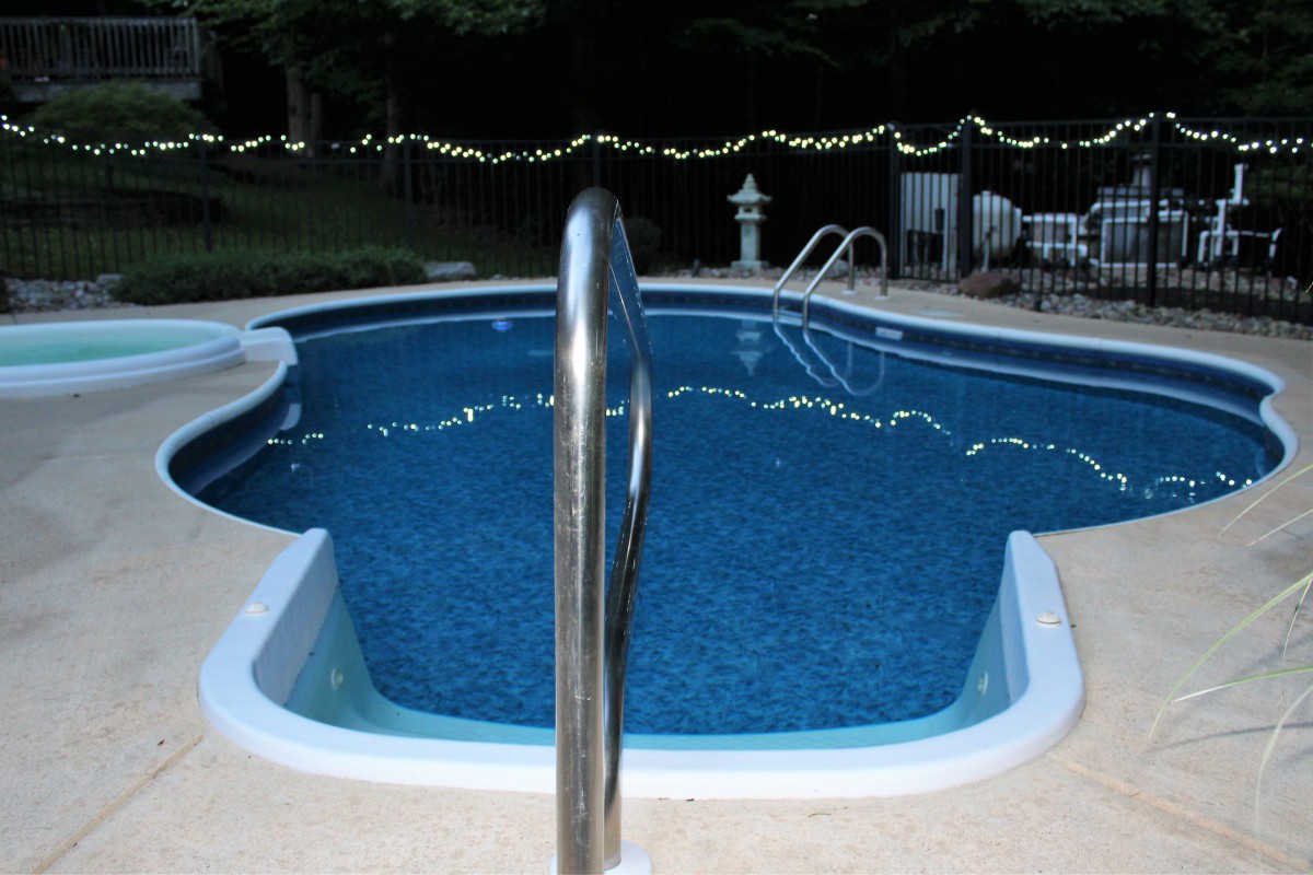 A serene outdoor swimming pool at night, illuminated by string lights.