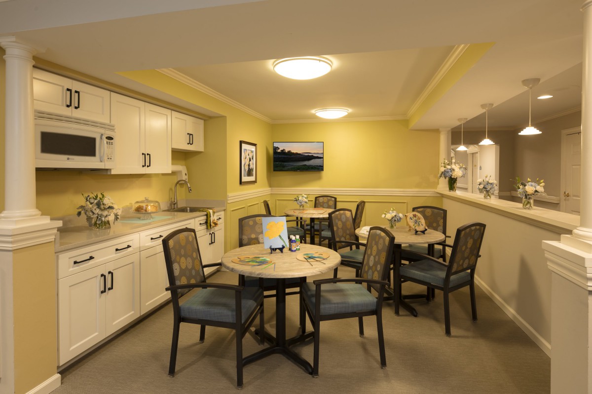 A cozy kitchen and dining area with round tables, comfortable chairs, and a mounted television.
