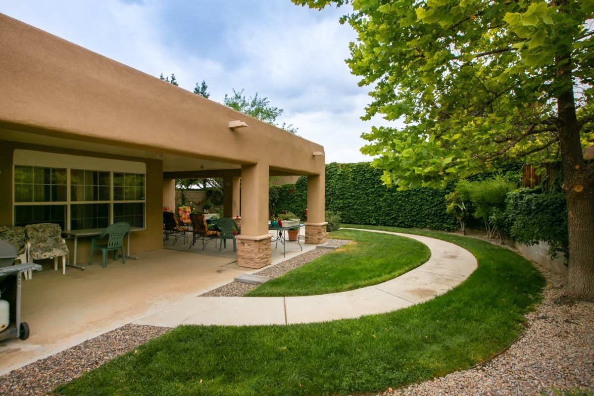 A serene backyard with a covered patio and well-maintained lawn.