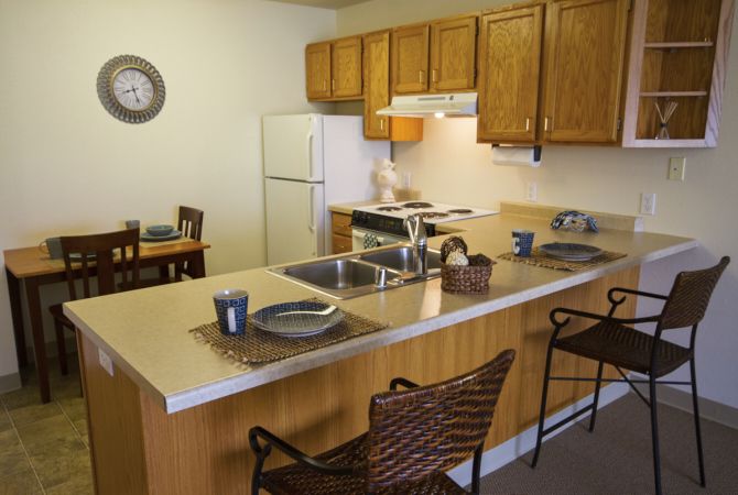 A cozy kitchen with a dining area, featuring wooden cabinets and a countertop with seating.