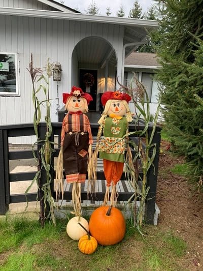 Festive scarecrows and pumpkins adorn the entrance to a house.