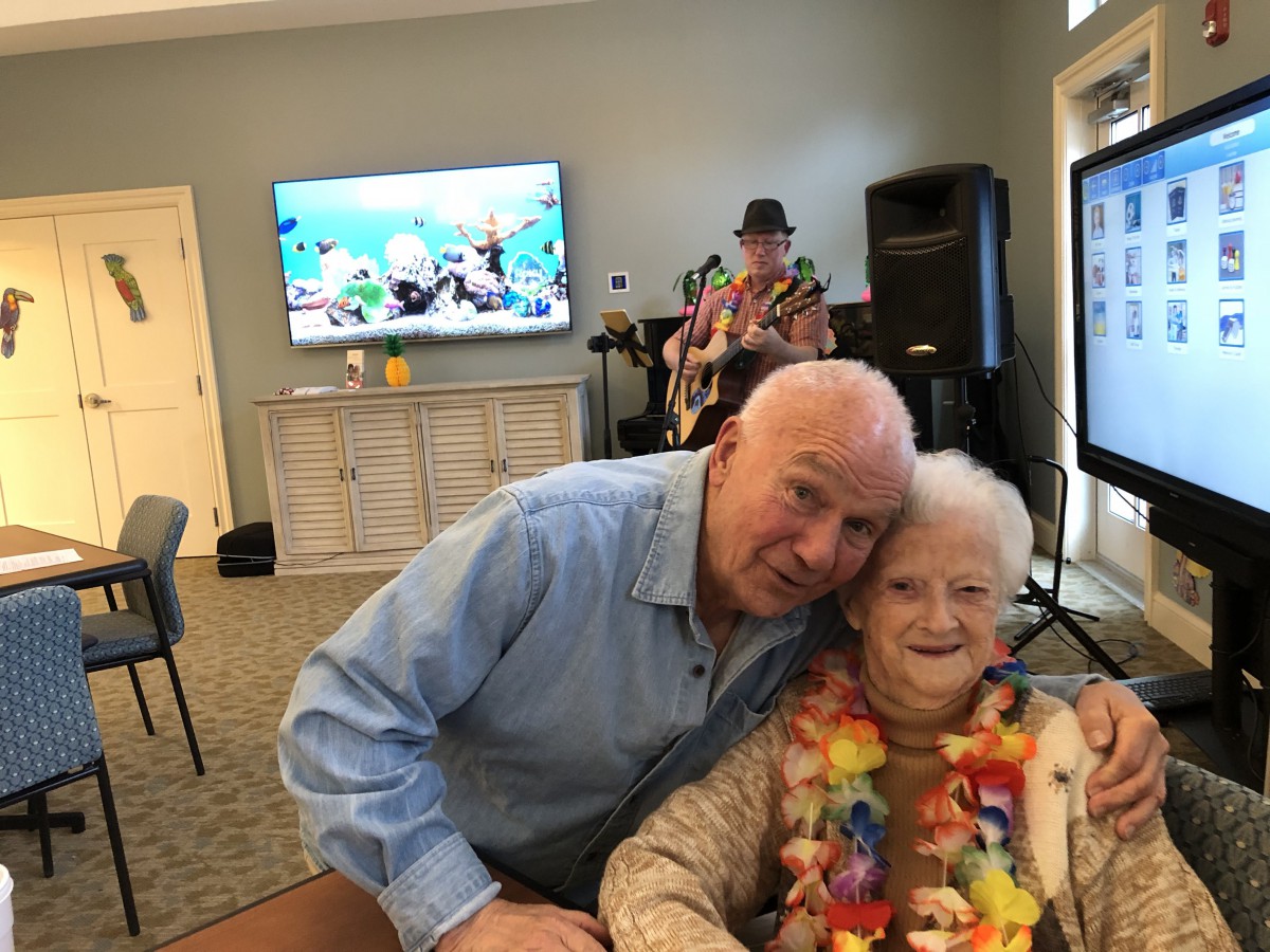 A man and an elderly woman celebrate together at a festive indoor event with music playing in the background.