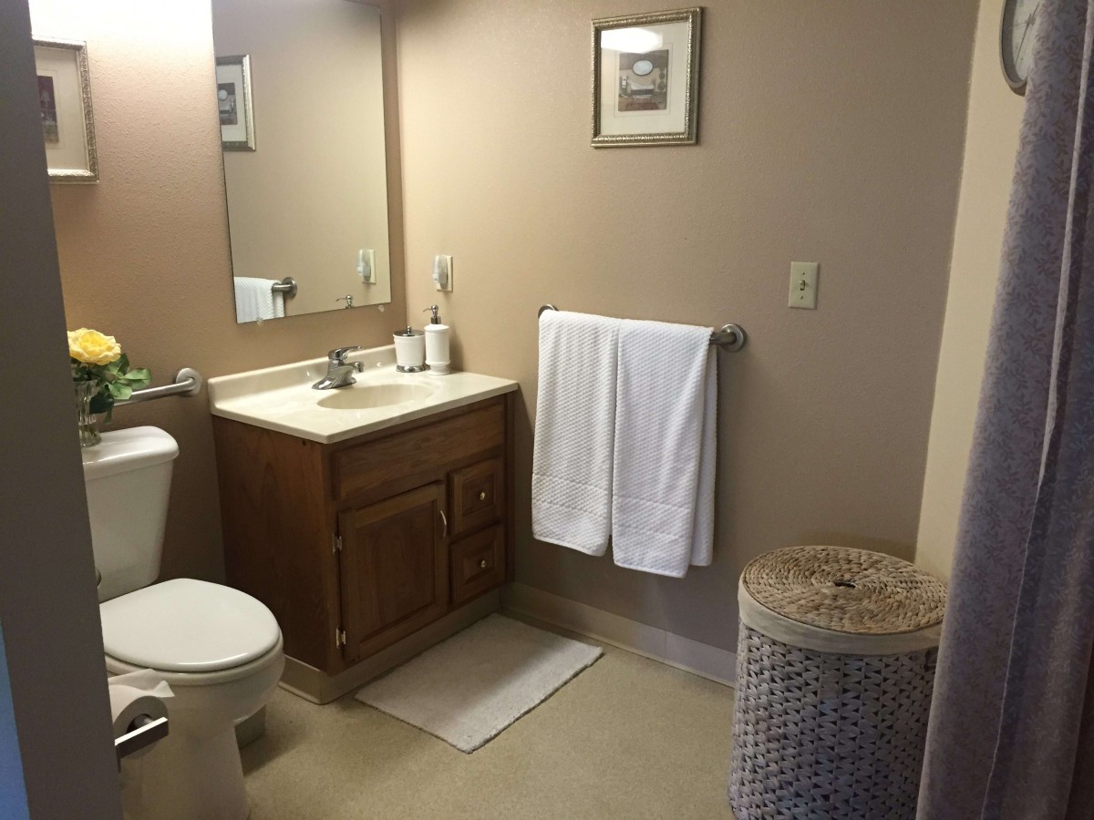 A neatly organized bathroom with a sink, toilet, towel, and laundry basket.