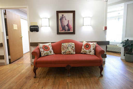 A cozy living room setup featuring a red sofa adorned with decorative pillows and framed artwork, illuminated by soft wall lights.