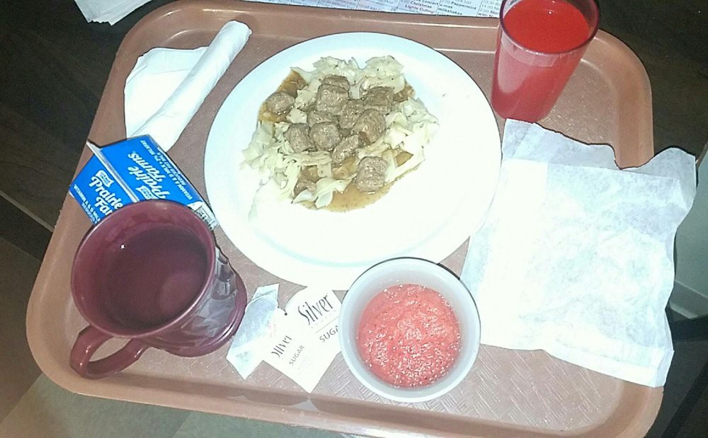 A hospital meal tray with beef stew, a red drink, and soup.
