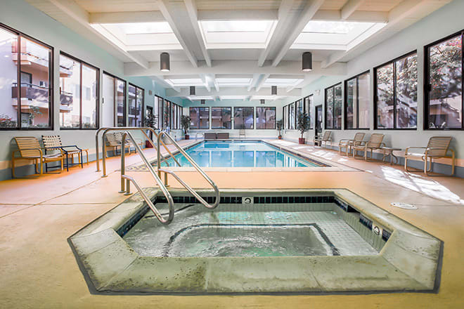 A serene indoor recreation area featuring a swimming pool and hot tub, with natural light streaming through skylights.