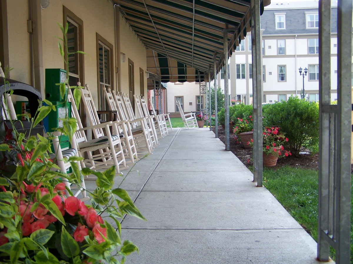 A covered porch with rocking chairs lined up alongside a building.