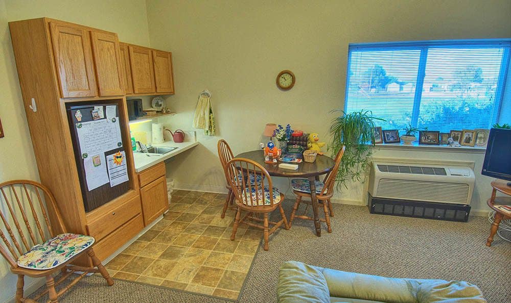 A cozy living area featuring a small dining table with chairs, a television, built-in cabinets, and an indoor plant.