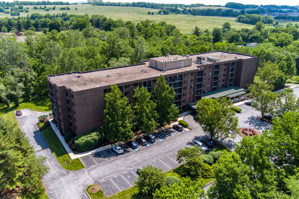 Aerial view of a residential apartment building surrounded by lush greenery and a parking lot.