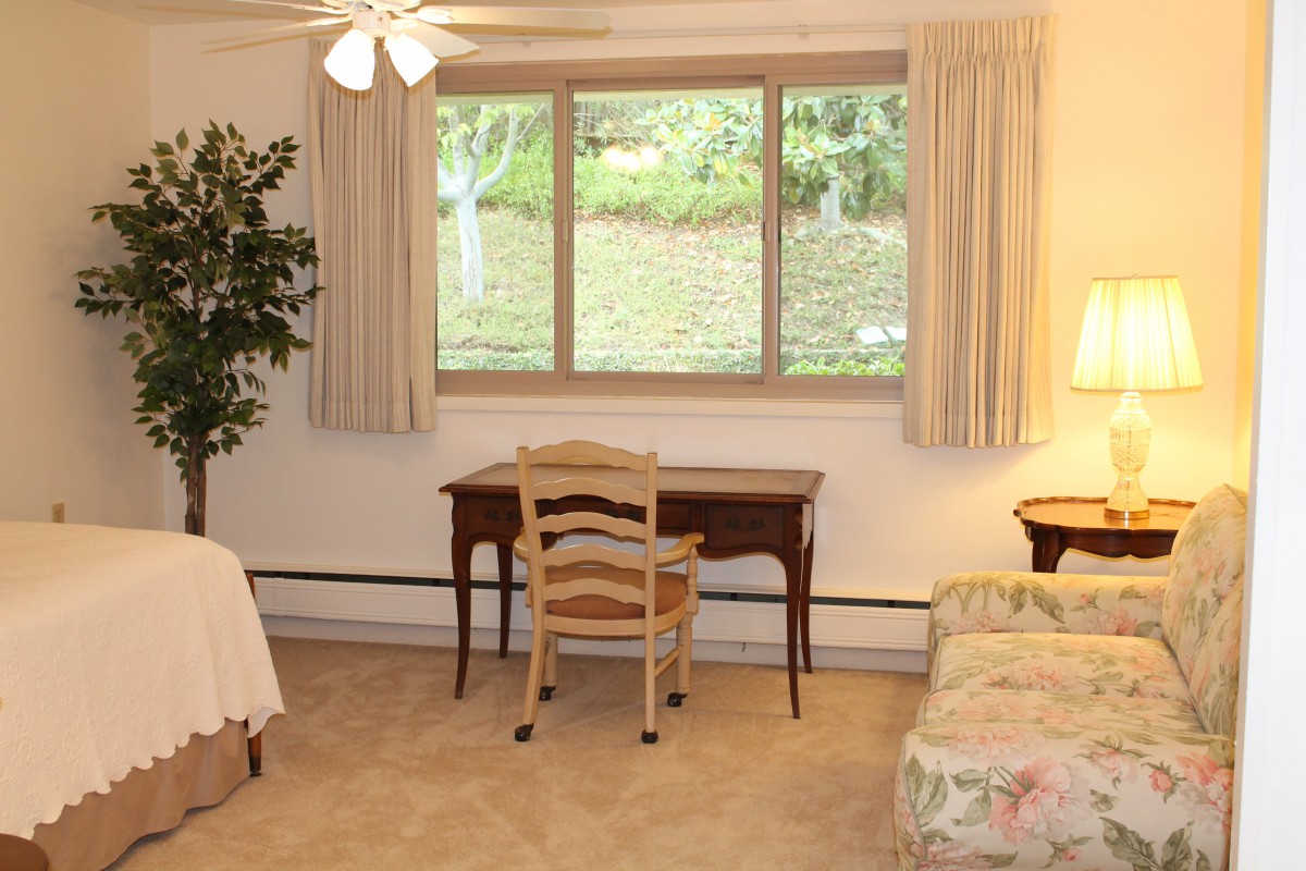 A cozy bedroom with a desk, chair, and large window overlooking greenery.
