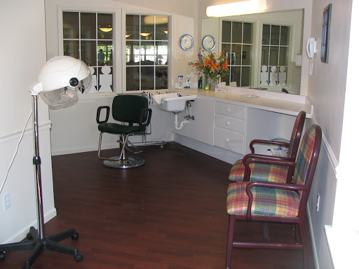 A cozy hair salon interior featuring a styling chair, waiting chairs, and natural light.