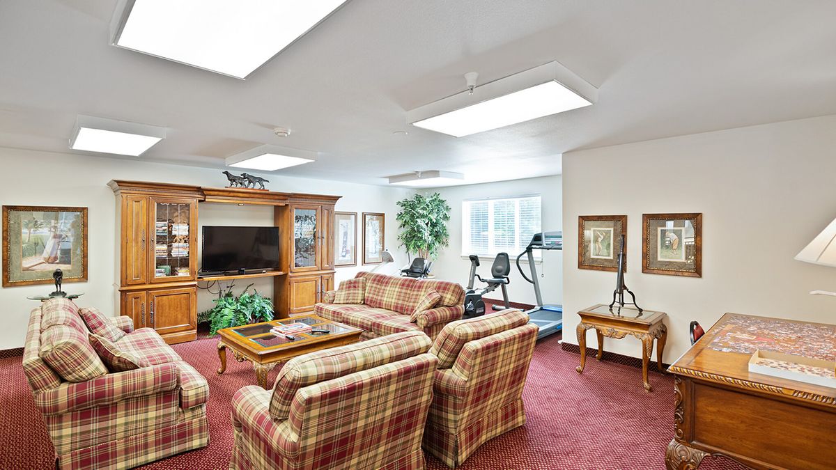 A cozy living room with plaid sofas, a large TV, and exercise equipment near a window.